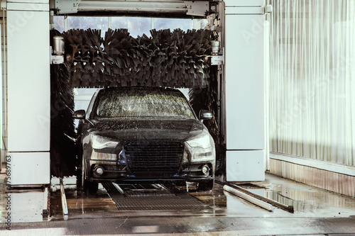 car wash automat with black vehicle drive through washing machine while cleaning and brushing the automobile with soap and water