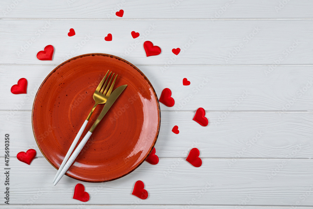 Valentines day table setting on a white wooden background top view, photo with copyspace. A red plate, golden cutlery and red hearts top view, romantic dinner concept Valentines day table setting on a white wooden background top view, photo with copyspace. A red plate, golden cutlery and red hearts top view, romantic dinner concept