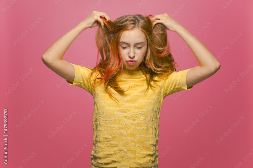Beautiful young girl ruffle long colored hairs closed eyes enjoying styling, perfect hair condition on pink background