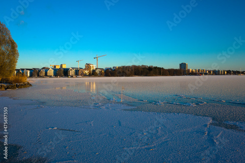 Winter day in Scandinavia, Frost covered ice of frozen lake Malaren, view of construction cranes in new residential area of Oster Malarstrand, Vasteras, Sweden