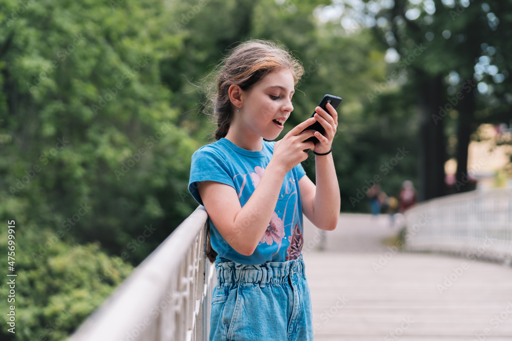 Little girl recording a voice message with her phone, in a park.