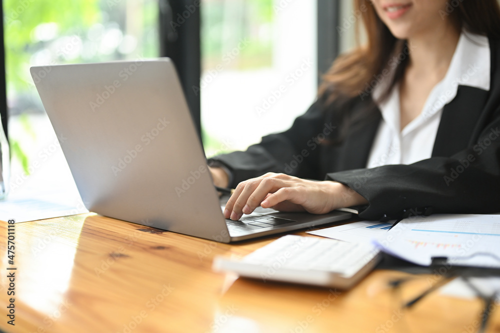 Photo of a beautiful insurance agent typing on a computer laptop at the wooden working desk surrounded by a document and office equipment. Photo of a beautiful insurance agent typing on a computer laptop at the wooden working desk surrounded by a document and office equipment.