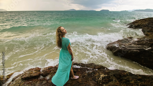 Woman walks on rock of sea reef stone, stormy cloudy ocean. Blue swimsuit dress tunic. Concept rest, tropical resort coastline tourism summer holidays © ivandanru