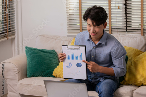 At home, an Asian businessman works on a desk with a laptop, searching for jobs and paperwork. photo