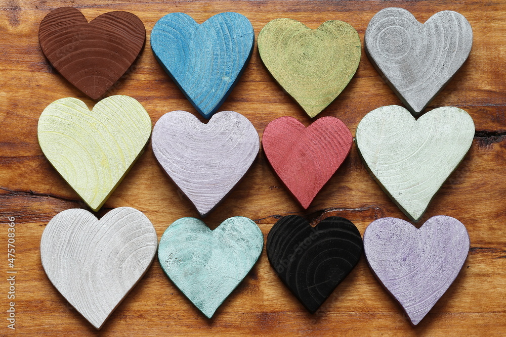 Multicolored hearts on a wooden background. Many wooden painted hearts in different colors. 