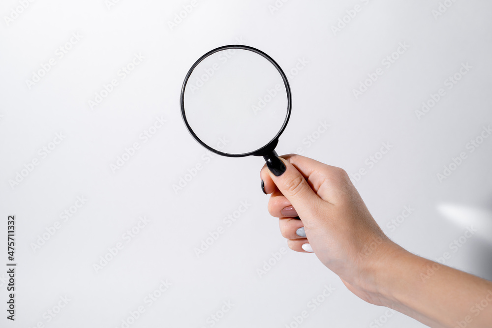 Female hand holding a magnifying glass with black frame on a white background Female hand holding a magnifying glass with black frame on a white background