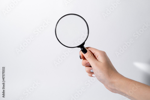 Female hand holding a magnifying glass with black frame on a white background