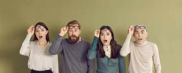 Four people gasp in surprise and take off their glasses when they see something unusual. Group of 4 young and old men and women standing in line and looking at something with shocked face expressions