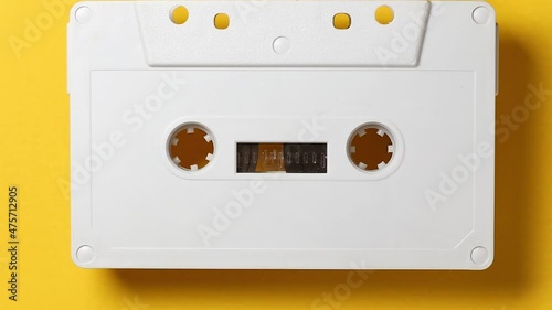 white audio cassette playing against a yellow background