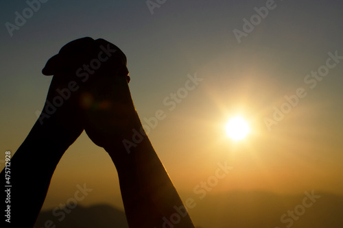 Praying hands with faith in religion and belief in God on sunset background. Power of hope or love and devotion.
