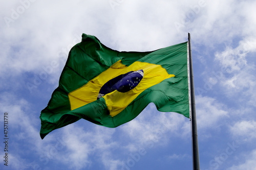 Brazilian flag blowing in the wind with blue sky and clouds.