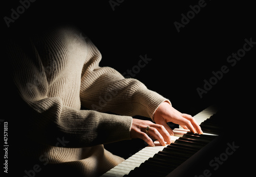 Female pianist in sweater dress plays chord on black piano with both hands. Touches gently the keyboard.