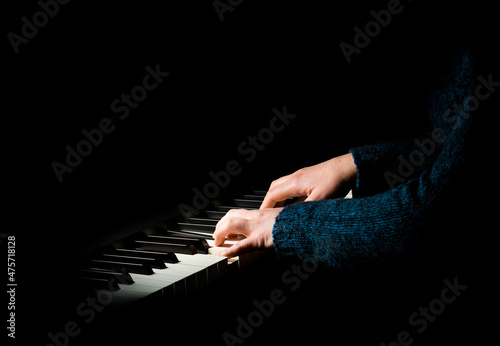Female pianist in blue sweater plays chord on black piano with both hands. Touches gently the keyboard.