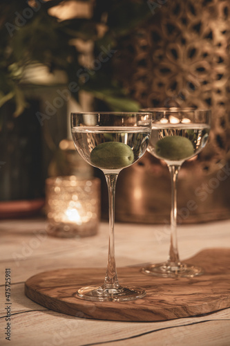 Close up shot of two martini cocktails with olive in beautiful, vintage pony glass. Bokeh lights in background. Indoor, cozy, warm festive atmosphere, slightly faded.