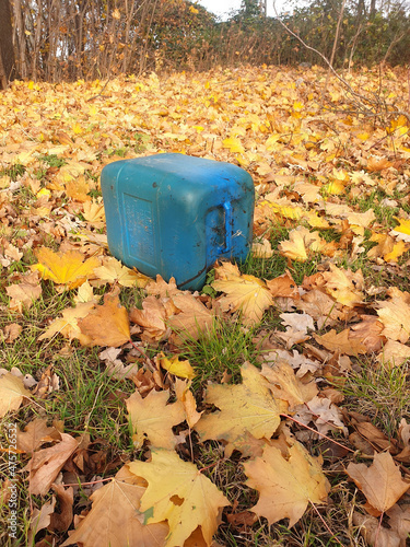 Blue,  plastic barrel of fuel n the ground surrounded by dried leaves photo