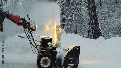 Snow-covered man cleans the road in winter with blower, snow removal equipment