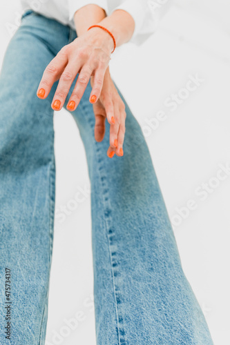 Girl in blue jeans with orange manicure and a bracelet on her arm
