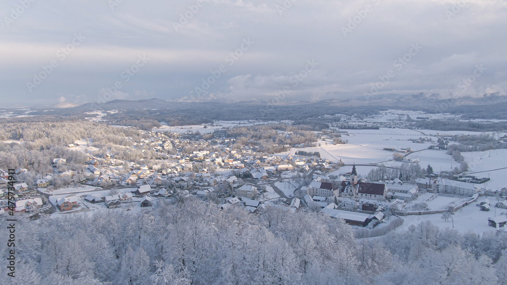 AERIAL: Winter morning sunbeams illuminate snowy valley and suburban village.