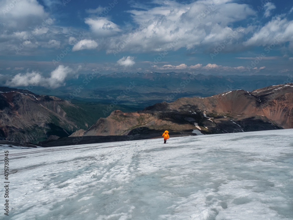 Solo hiker on the glacier. Extreme recreation and mountain tourism. A male hikers down the mountain path. In the background, large snow-capped mountains. Solo hiker on the glacier. Extreme recreation and mountain tourism. A male hikers down the mountain path. In the background, large snow-capped mountains.