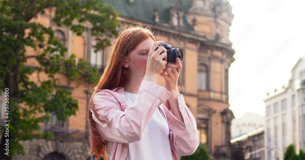 Pretty female lady walking on street in city, taking pictures and looking at antique buildings. Redheaded girl photographer using digital camera. Technology, tourism, traveling concept. Pretty female lady walking on street in city, taking pictures and looking at antique buildings. Redheaded girl photographer using digital camera. Technology, tourism, traveling concept.