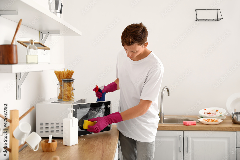Young man cleaning microwave with sponge in kitchen Young man cleaning microwave with sponge in kitchen