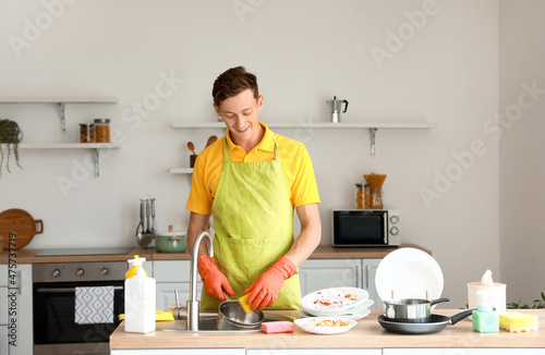 Young man cleaning cooking pot with sponge in kitchen