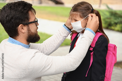 Man helping his little daughter to put on medical mask before school