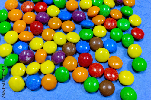 Scattered colored candies on a blue background. Lots of colored sweets on a blue surface
