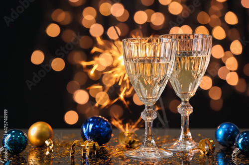 Glasses with champagne and Christmas decorations on table against blurred lights photo
