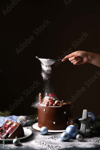 Cuadro en lienzo Woman decorating tasty Christmas chocolate cake with powdered sugar on dark back