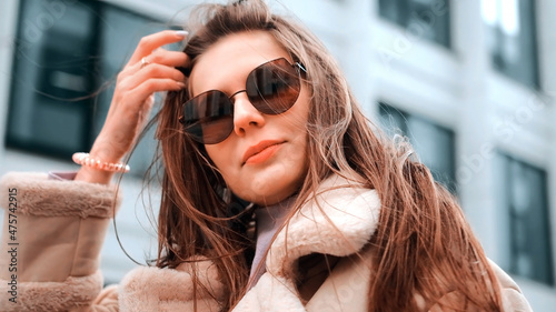 A girl in a beige jacket and glasses walks down the street in the business district of the city, a strong wind. Success