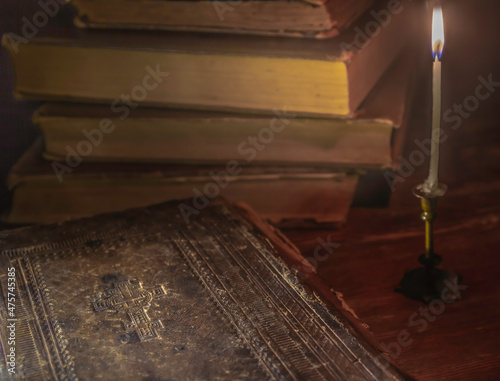 Candle in candlestick illuminates cover of old bible and books in the background