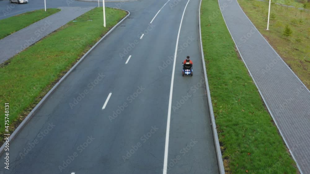 Aerial view of a caucasian man with amputated legs and arms drives on electric wheelchair along the empty asphalt road Aerial view of a caucasian man with amputated legs and arms drives on electric wheelchair along the empty asphalt road