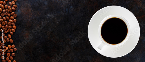 Cup of black coffee on a white saucer and coffee beans. Coffee and roasted coffee beans on a dark background. Coffee background. Panoramic shot