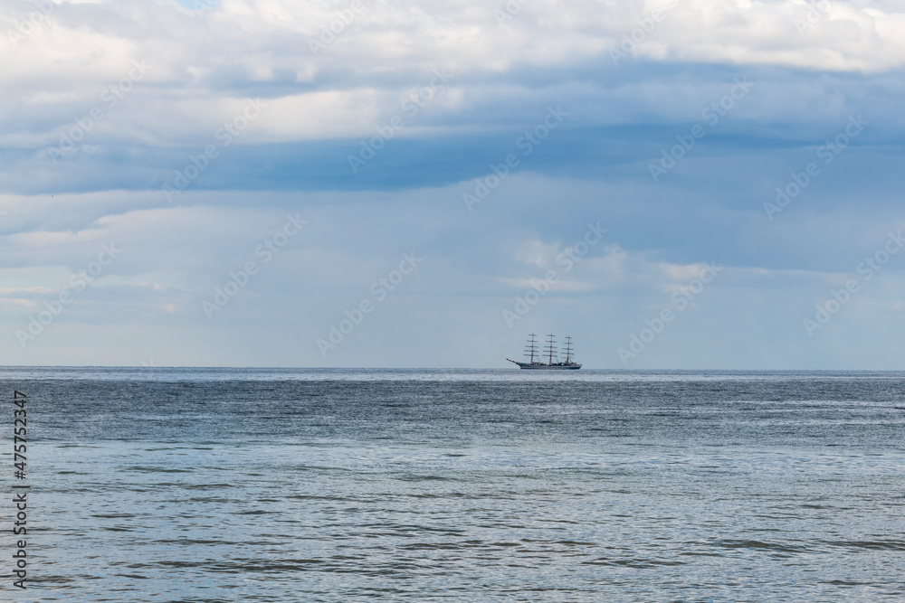 Large sailboat in the sea on the horizon against the backdrop of a cloudy sky