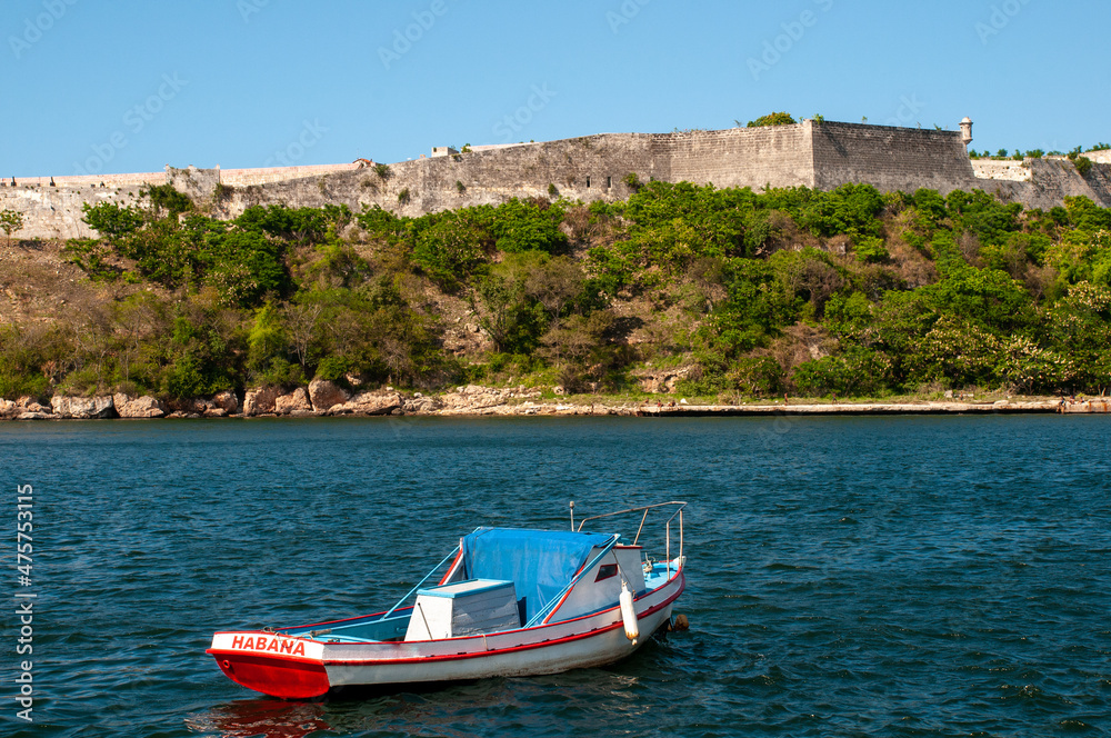 Fishing boat anchoring at the entrance to the port of Havana with the wall of a fort from the Spanish colonial era in the background. Cuba.