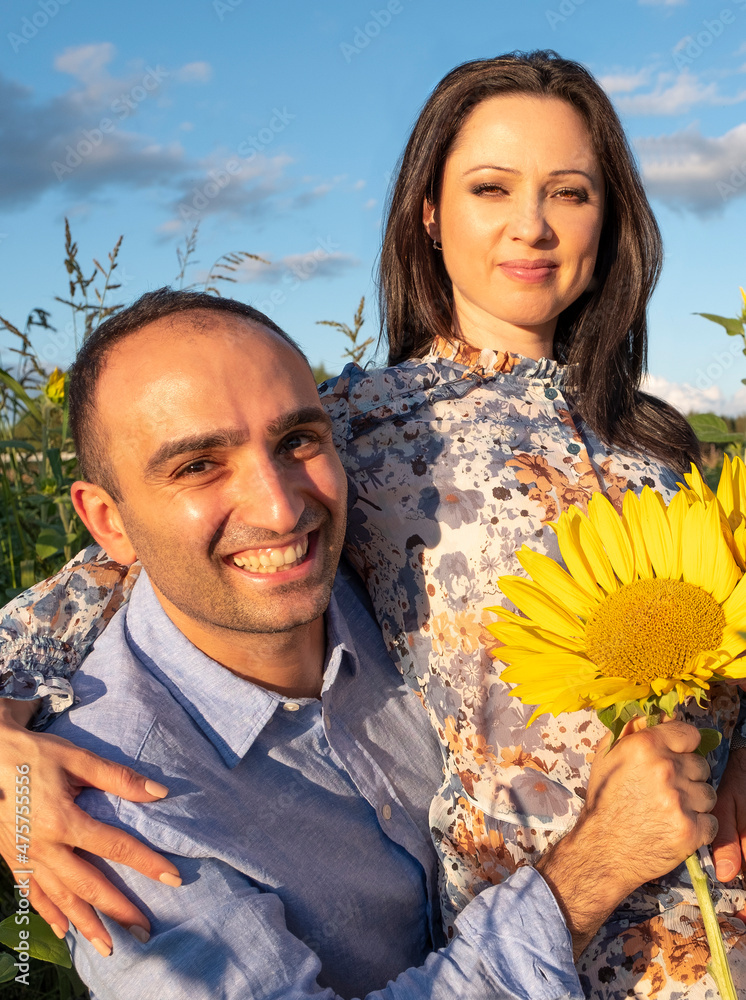 Φωτογραφία A man and a young woman are sitting in a field of sunflowers, smiling and looking at the camera