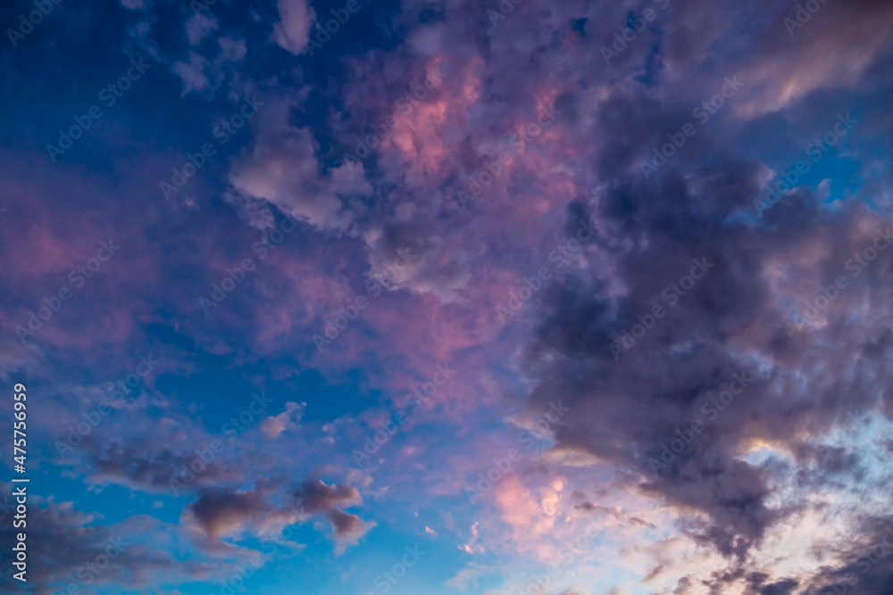 White and dark clouds colored pink on blue sky during sunset
