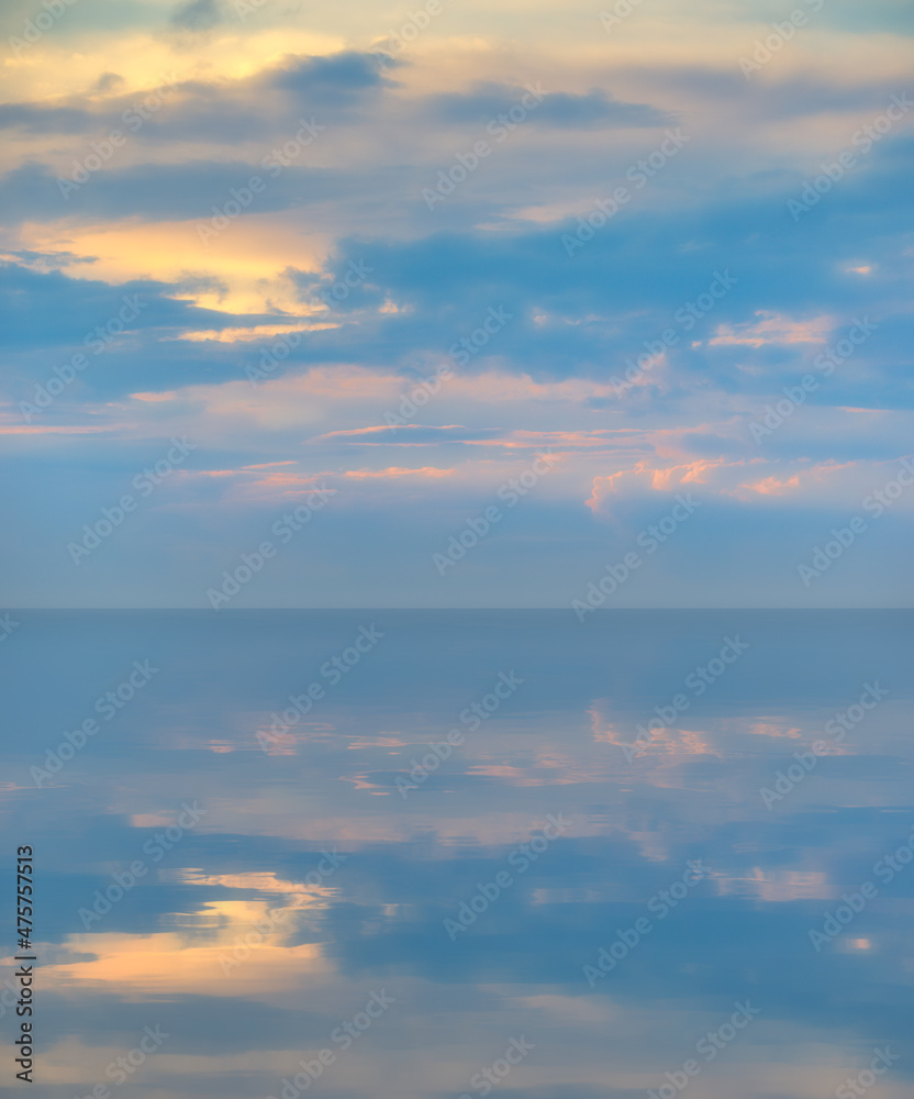 Soft blue and yellow clouds near sunset with reflection on calm sea water surface Soft blue and yellow clouds near sunset with reflection on calm sea water surface