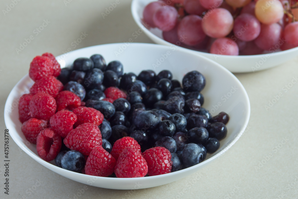A close-up of a few raspberries in several plates with fruits of the forest on a textured surface. Natural ingredients and healthy food. A close-up of a few raspberries in several plates with fruits of the forest on a textured surface. Natural ingredients and healthy food.