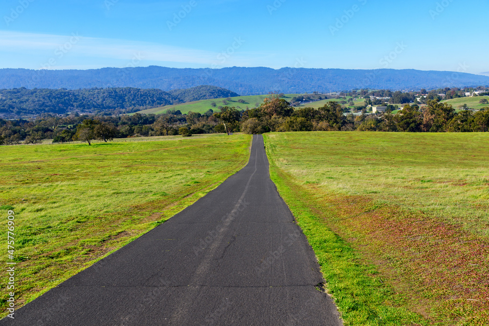 Obraz premium Stanford Dish Loop paved hiking trail going to distant hills between green grass fields in winter