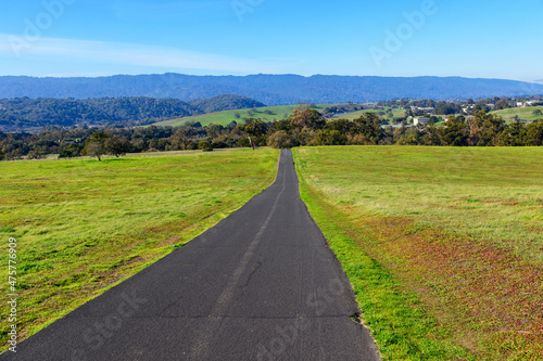 Stanford Dish Loop paved hiking trail going to distant hills between green grass fields in winter