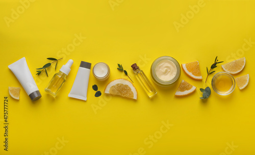 Body cream and other cosmetic products with ingredients on yellow background, flat lay