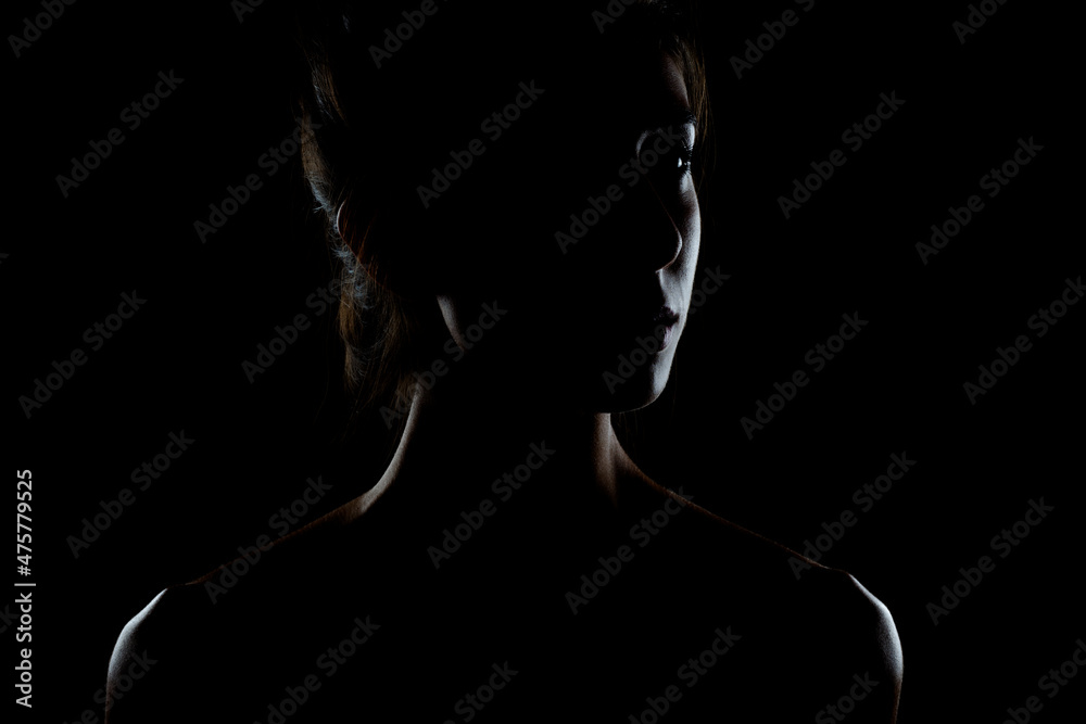 silhouette contour of a beautiful brunette girl. Side lit studio portrait on dark background.