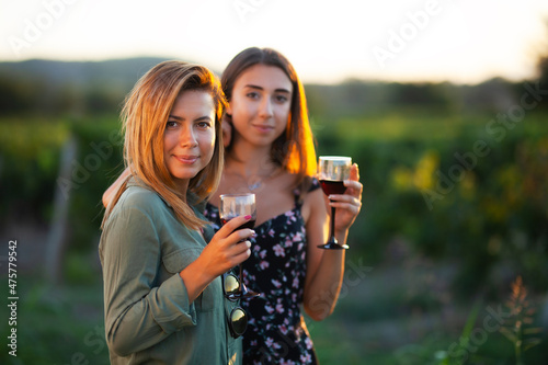 Beautiful girls tasting wine in a field near vineyard field. Celebrating successful harvest season. Couple having a romantic date. Rural tourism concept