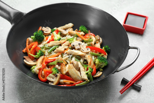 Stir fried noodles with mushrooms, chicken and vegetables in wok on light grey table photo