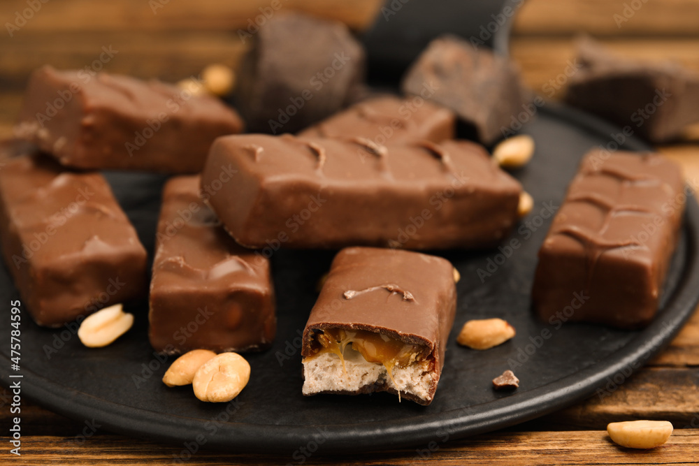 Slate board of chocolate bars with caramel, nuts and nougat on wooden table, closeup