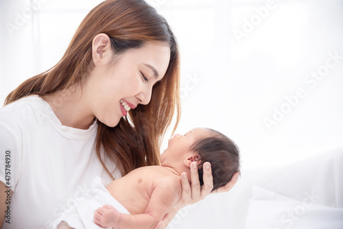 Asian loving mom carying of her newborn baby at home. Happy mum holding sleeping infant child on hands. Mother hugging her little one months old son.