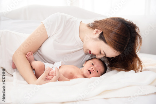 Asian loving mom carying of her newborn baby at home. Happy mum holding sleeping infant child on hands. Mother hugging her little one months old son.