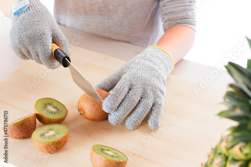 Closeup of a kid cutting kiwis with gloves on a wooden board